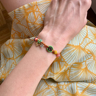 Handgefertigtes Makramee-Armband mit Smiley-Perle, bunten Miyuki-Perlen und kleinen Blumenanhängern in Orange, Grün und Rosa.