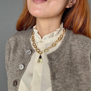 Frau mit goldener Gliederkette und Bienenanhänger, getragen über cremefarbener Bluse und grauer Strickjacke – Produktfoto der Golden Bee Halskette