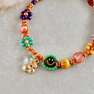 Handgefertigtes Makramee-Armband mit Smiley-Perle, bunten Miyuki-Perlen und kleinen Blumenanhängern in Orange, Grün und Rosa.