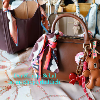 Braune Handtasche mit buntem Skinny-Schal am Griff und einem braunen Teddy-Schlüsselanhänger aus Leder, dekoriert mit farbigen Bändern und Charms.