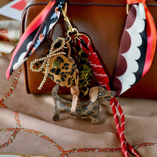 Dackel Taschenanhänger aus Kunstleder mit Mini-Leoparden-Täschchen und pink-braunem Satin-Schal an einer schwarzen Handtasche.