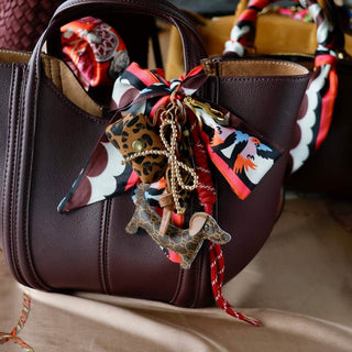 Dackel Taschenanhänger aus Kunstleder mit Mini-Leoparden-Täschchen und pink-braunem Satin-Schal an einer schwarzen Handtasche.