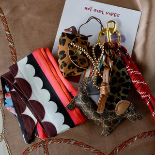 Set aus Dackel-Anhänger, Mini-Leopardentasche und Satin-Schal in warmen Braun- und Rottönen, dekorativ arrangiert.