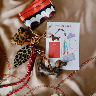 Set aus Dackel-Anhänger, Mini-Leopardentasche und Satin-Schal in warmen Braun- und Rottönen, dekorativ arrangiert.